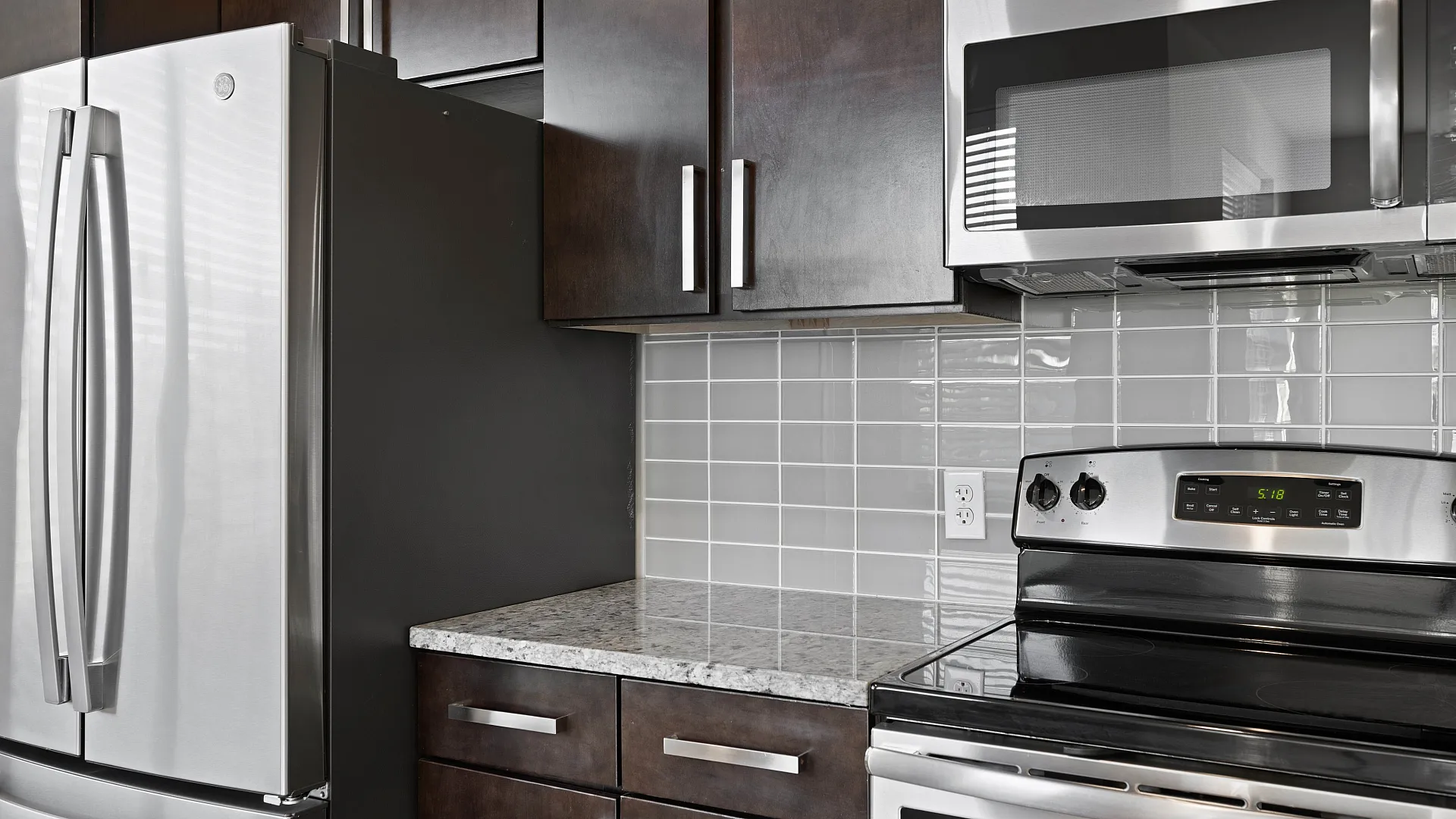 Modern kitchen featuring sleek stainless steel appliances, granite countertops, and stylish dark cabinetry.