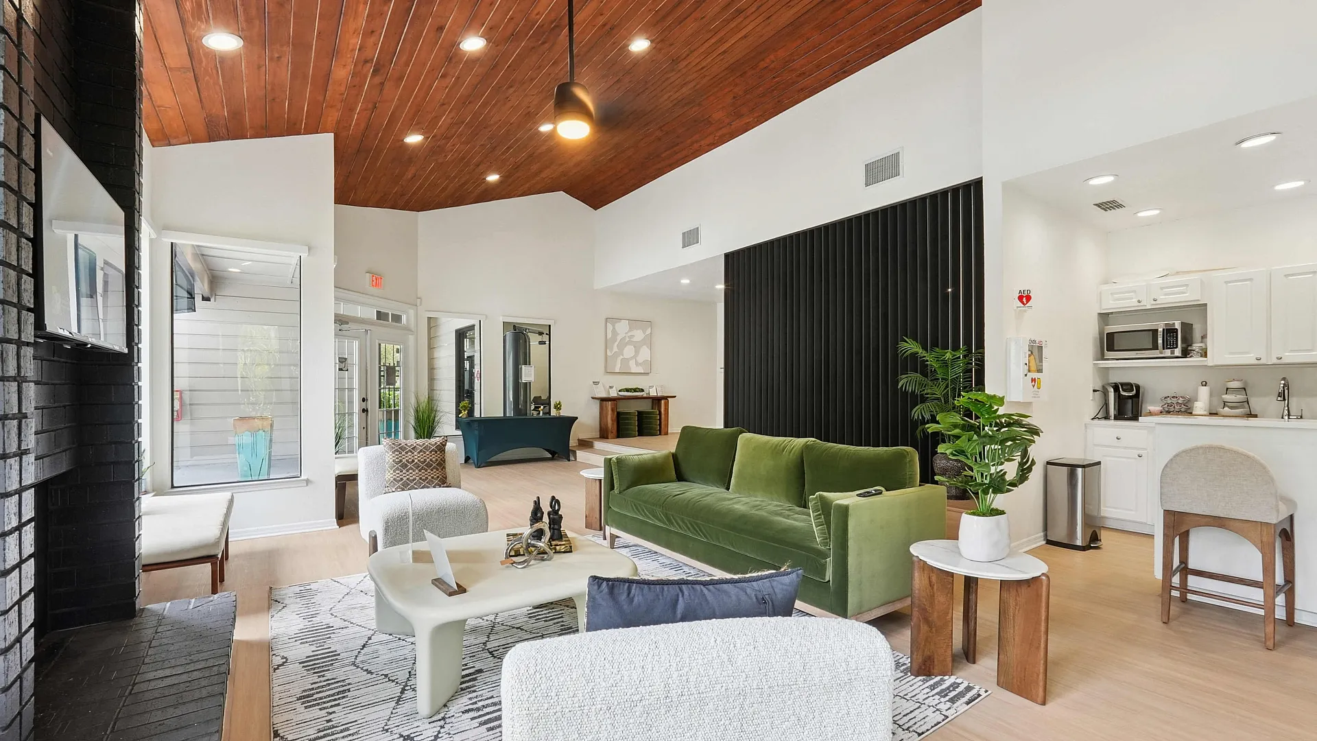 Chic modern living room with high wooden ceiling, featuring a vibrant green sofa, cozy white armchairs, and a sleek kitchenette for convenient living.