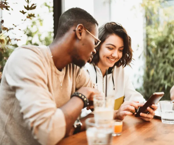 Two people enjoying a casual coffee meeting at a cozy cafe, surrounded by vibrant greenery and natural light.