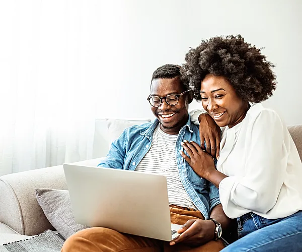 Happy couple enjoying a cozy moment on a comfortable couch, sharing a laptop in a bright and inviting living room.
