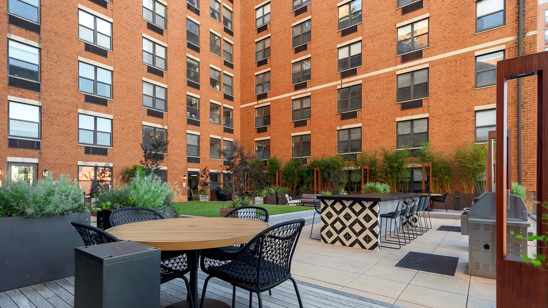 Chic outdoor courtyard with modern seating, lush greenery, and barbecue area set against a stylish brick apartment facade.