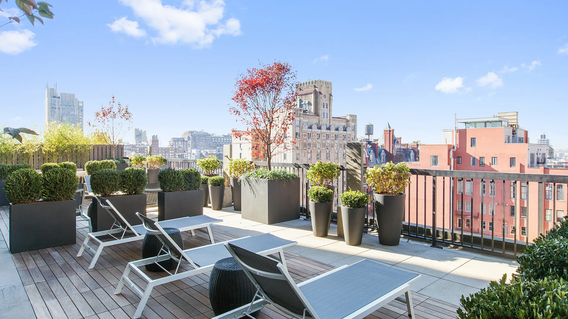 Luxurious rooftop terrace showcasing modern lounge chairs, lush planters, and scenic city views under a radiant blue sky.