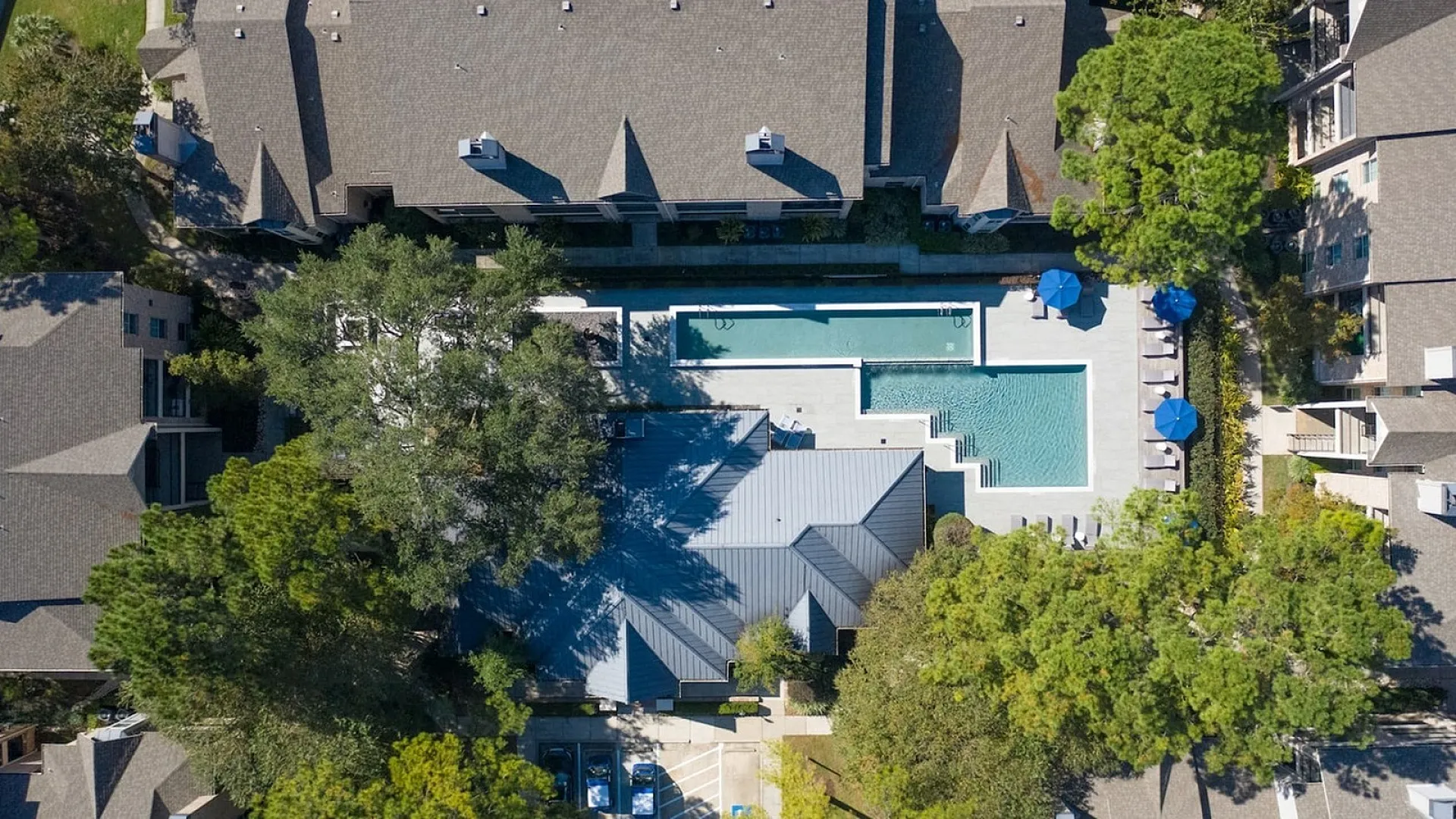Aerial view of a stunning residential complex featuring a sleek swimming pool surrounded by lush greenery and modern buildings with elegant rooftops.