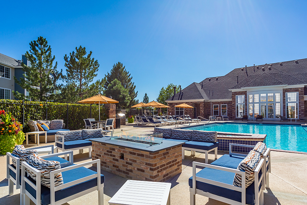 Luxurious outdoor pool area with stylish lounge chairs and cozy fire pit, surrounded by lush greenery and vibrant umbrellas.