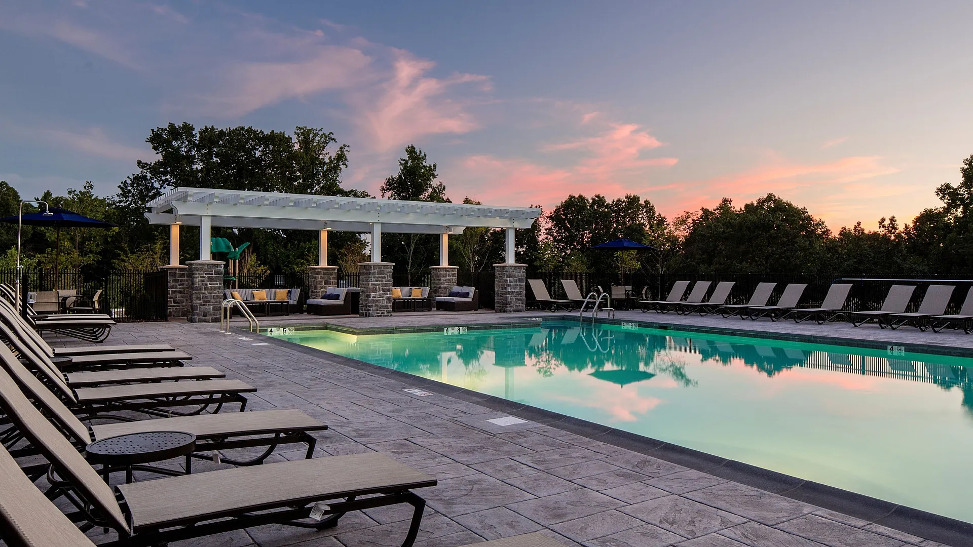 Luxurious outdoor pool area featuring elegant lounge chairs and a stylish pergola at sunset.