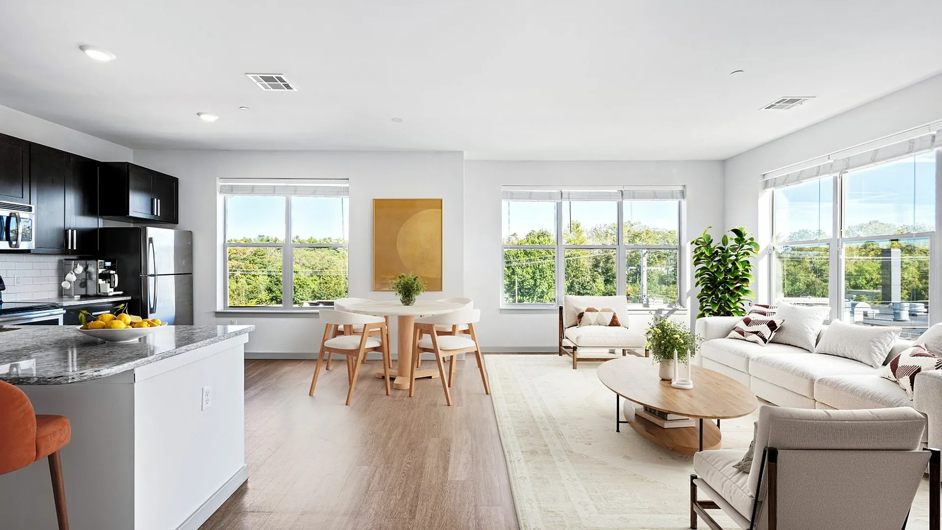 Bright, open-concept living and dining area with modern kitchen, large windows, and lush green views.