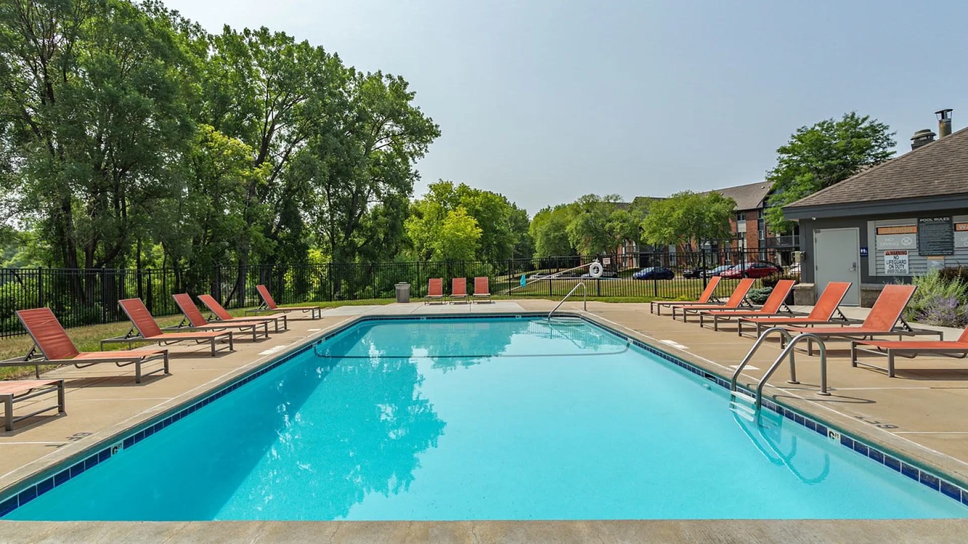 Inviting outdoor pool area with comfortable lounge chairs and lush greenery, perfect for relaxation and summer enjoyment.