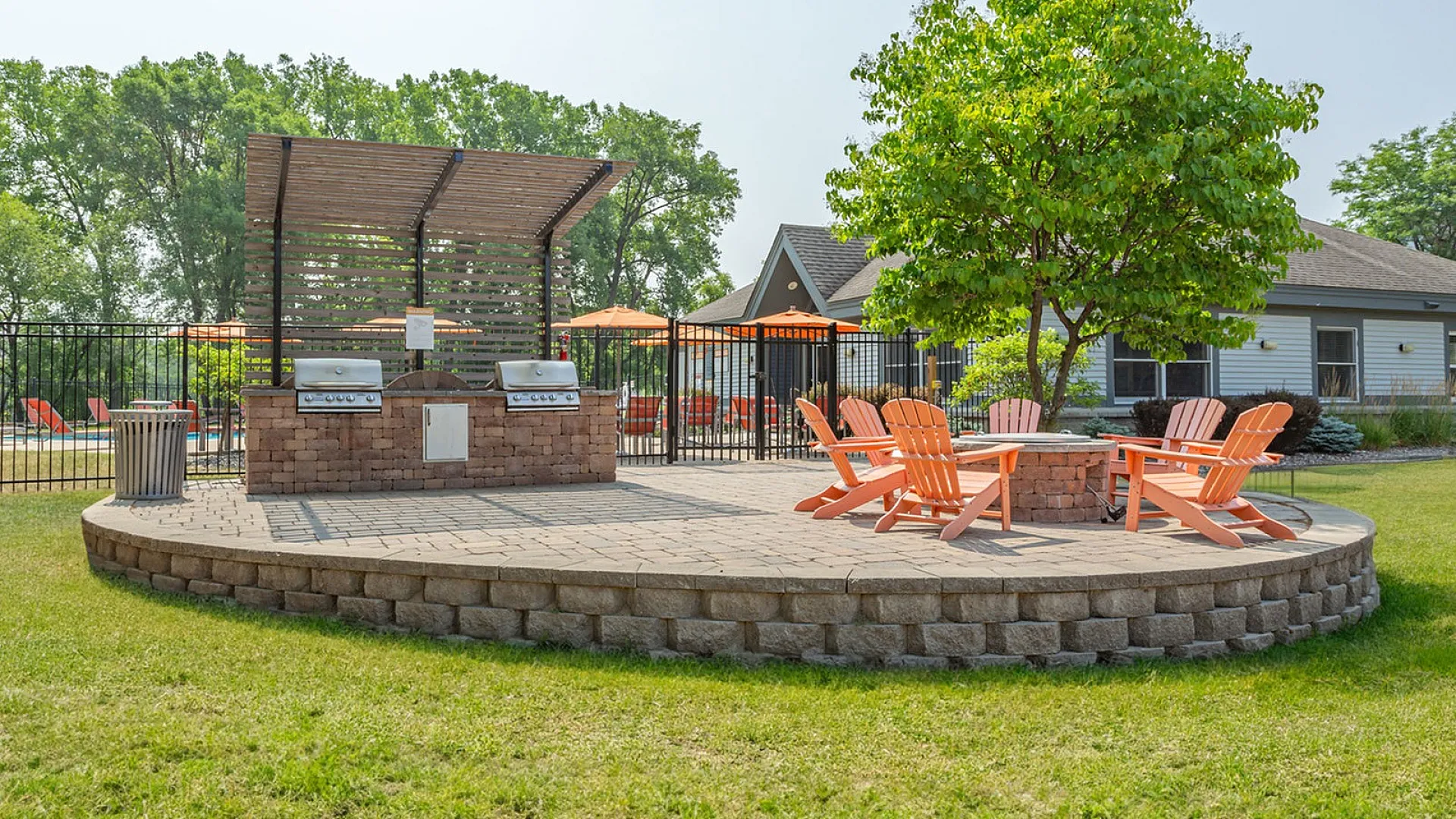 Charming outdoor patio with vibrant orange chairs and dual grills, nestled in lush greenery for perfect summer gatherings.