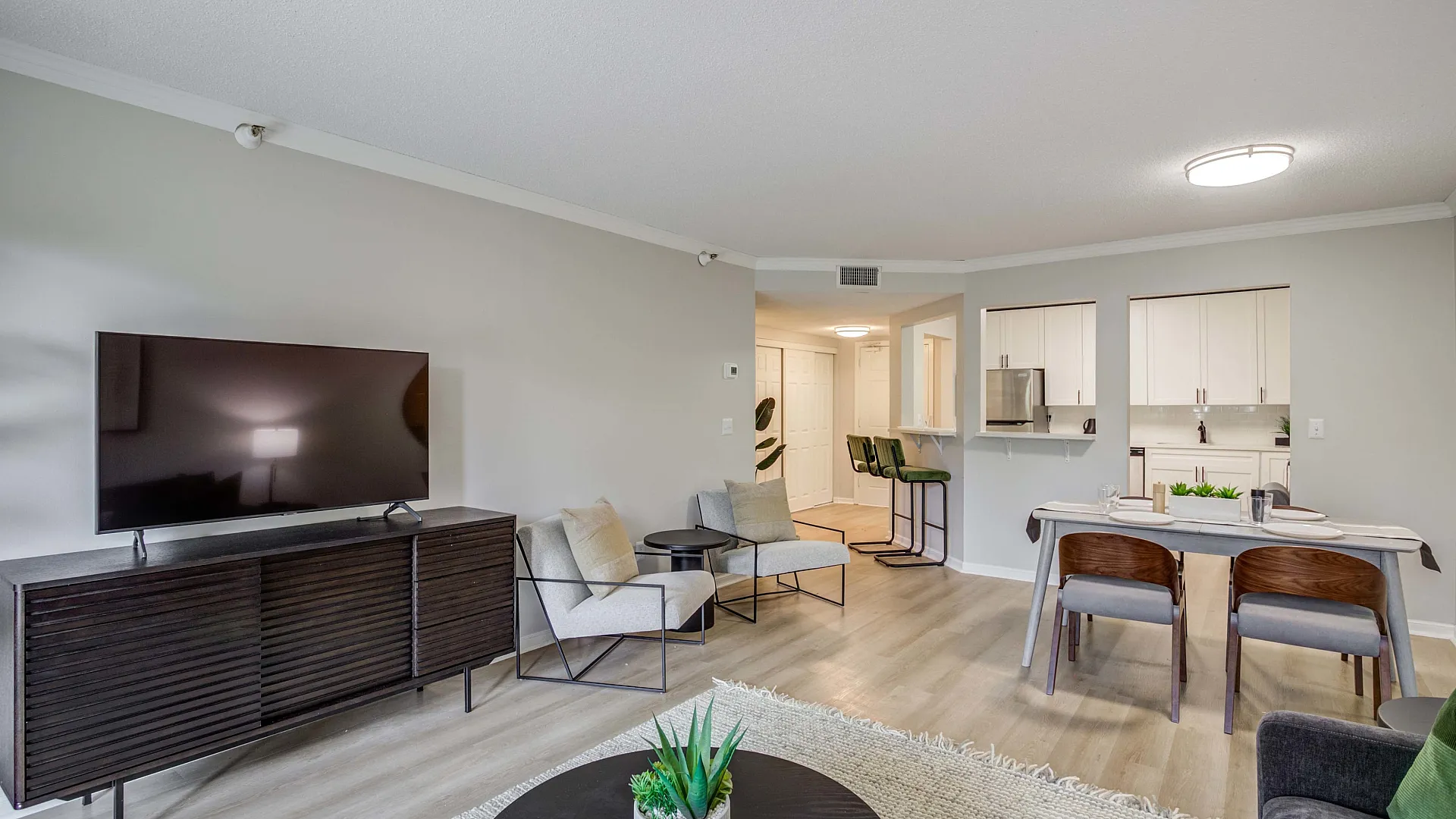 Contemporary open-concept living room with sleek furniture, a flat-screen TV, and a cozy dining area adjacent to a modern kitchen.