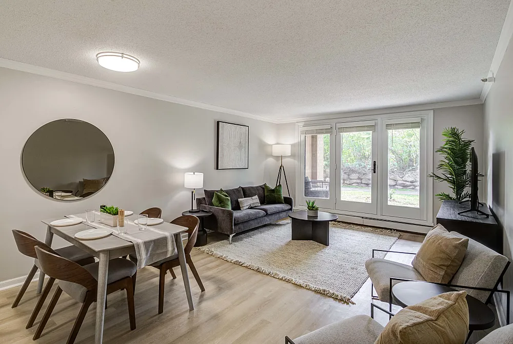 Bright and inviting living room with modern decor, featuring a cozy gray sofa, elegant dining area, and large windows offering a serene garden view.