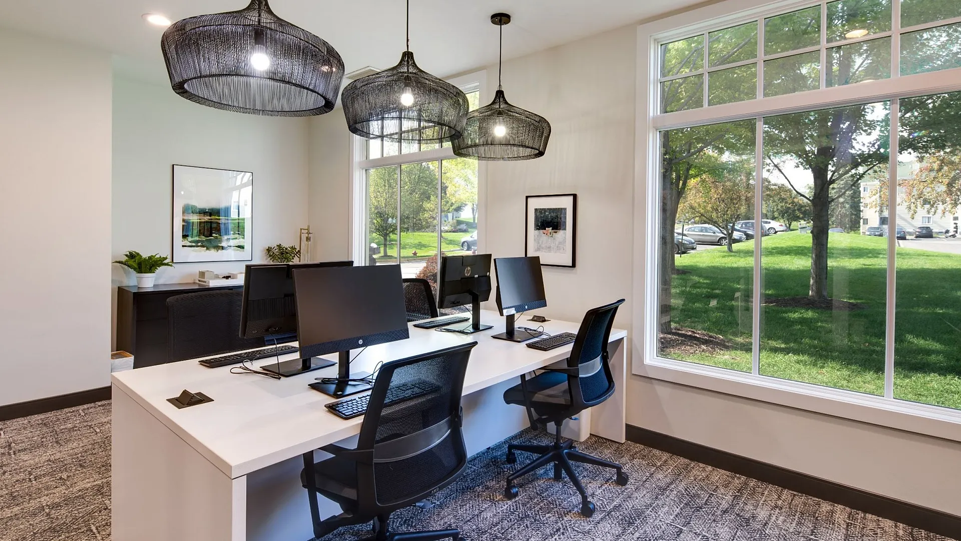 Bright and modern workspace featuring sleek desks, large windows with a green view, and chic pendant lighting.