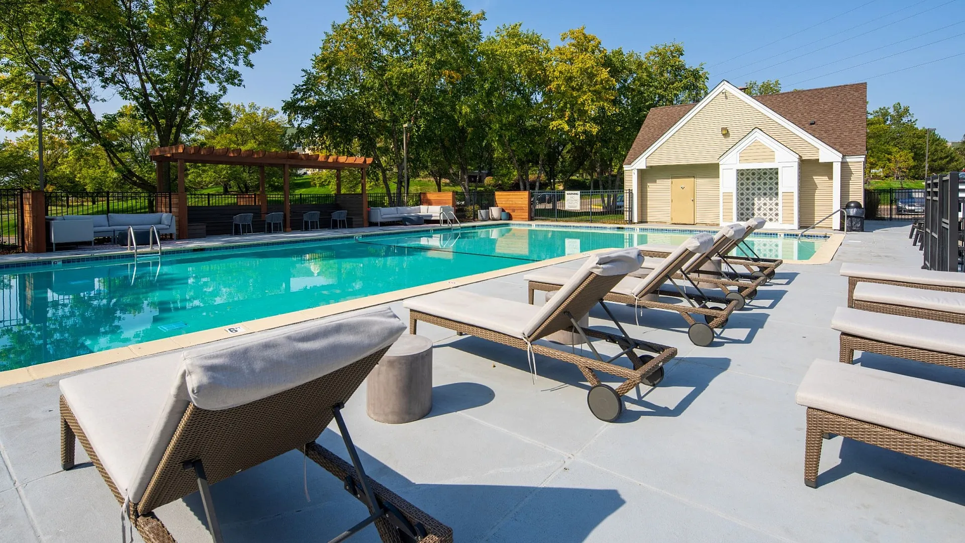 Inviting outdoor swimming pool area with comfortable loungers, surrounded by lush greenery and a charming pool house.