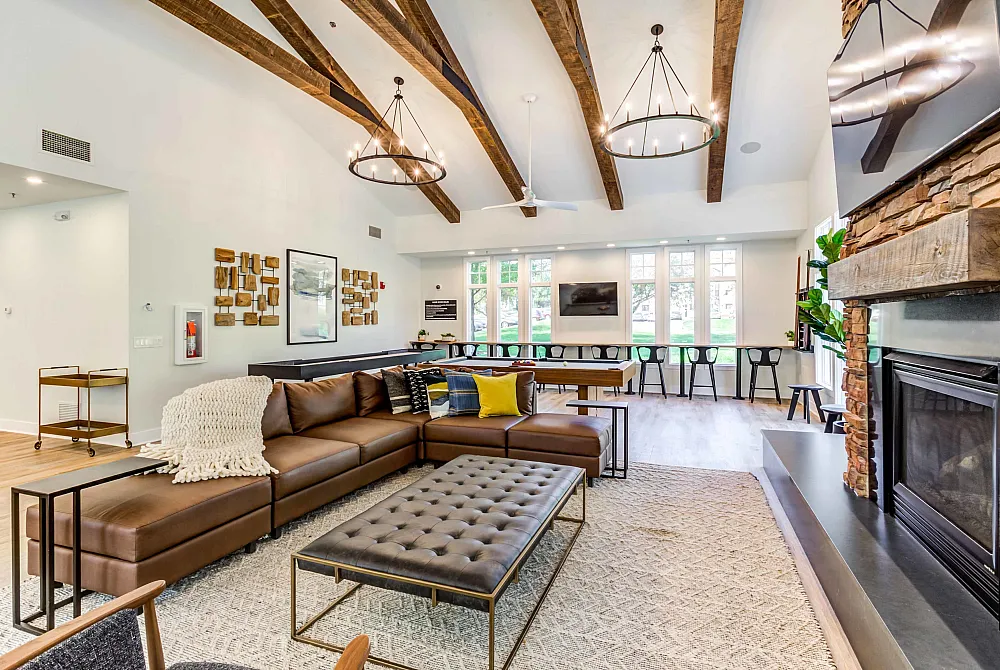Inviting living room with a modern design featuring a cozy brown leather sectional, elegant chandeliers, and a warm stone fireplace.