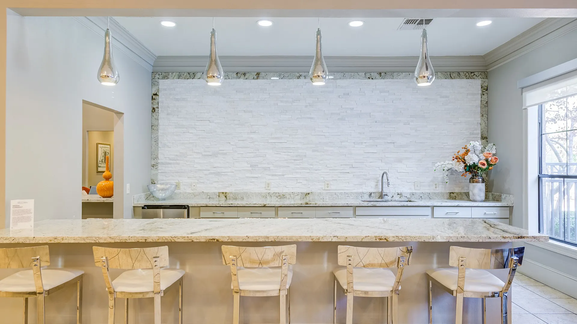 Elegant kitchen with modern pendant lights over a sleek marble countertop, offering chic bar seating and a stylish backsplash.