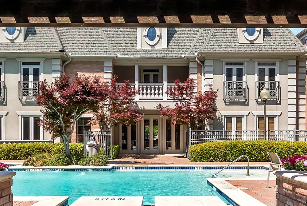 Luxurious apartment view featuring a sparkling pool, elegant architecture, and vibrant landscaping under a charming wooden pergola.