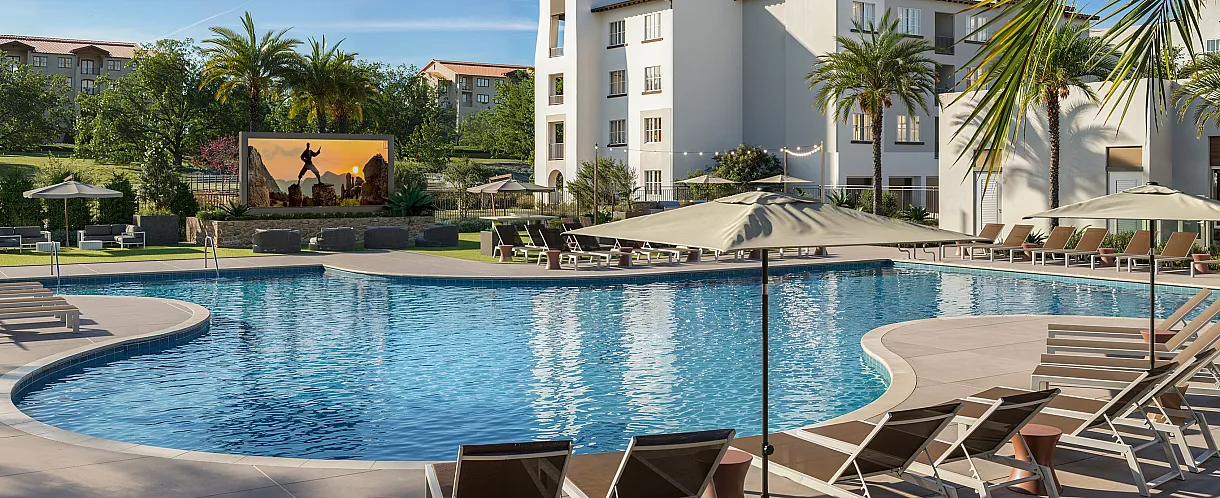 Luxurious outdoor pool area with stylish sun loungers, shaded umbrellas, and palm trees, offering a serene oasis for relaxation amidst beautiful architecture.
