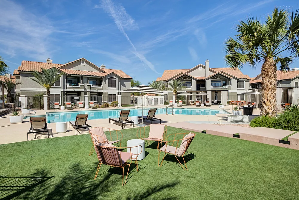 Luxurious apartment complex featuring modern buildings with a stunning pool, surrounded by lush green grass and palm trees, perfect for relaxing or entertaining.