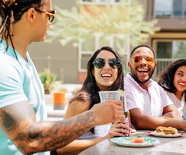 Lively group of friends enjoying a sunny day, laughing and dining outdoors, showcasing a vibrant social community setting.