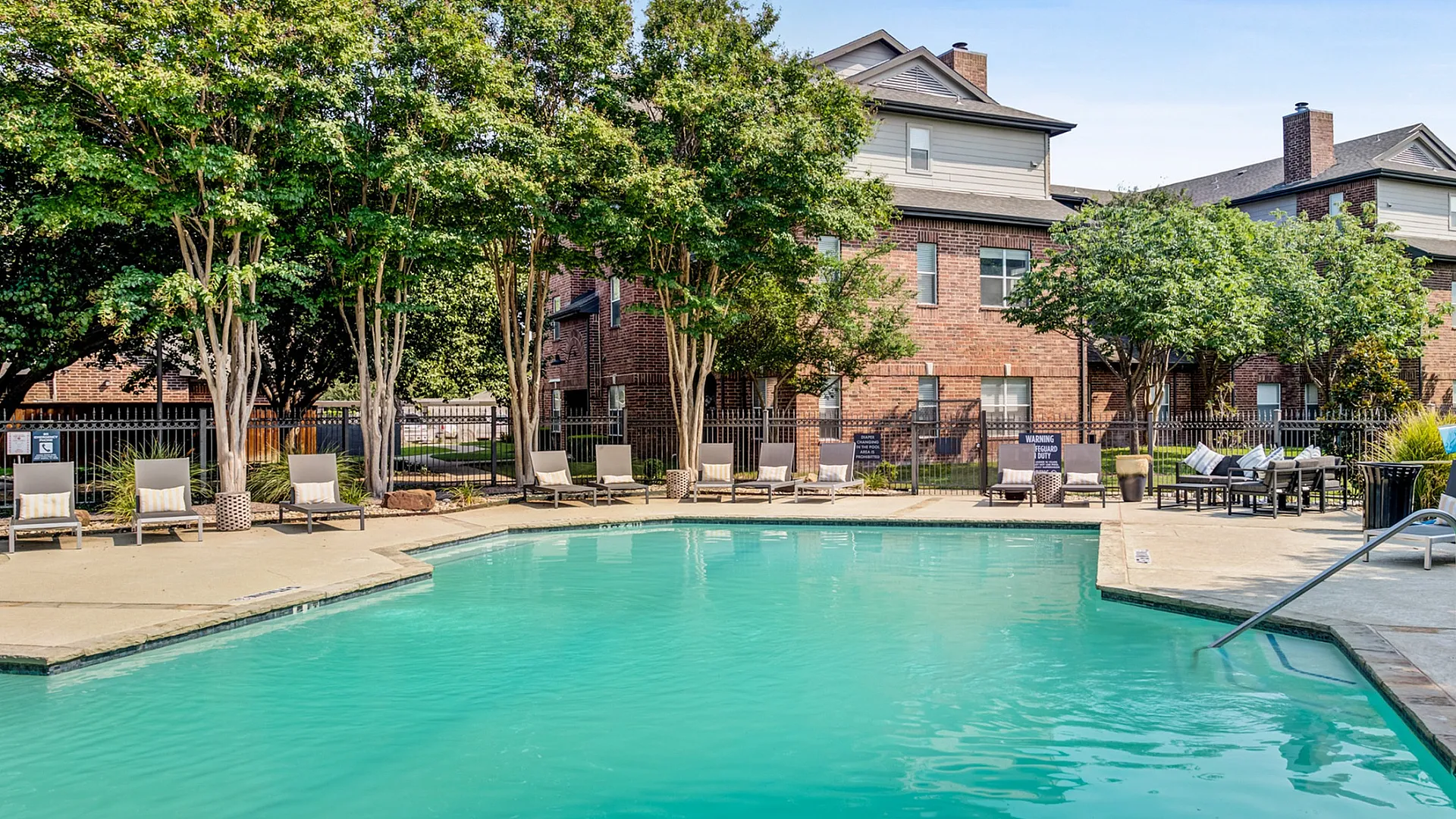 Inviting outdoor pool area surrounded by lush trees and comfortable lounge chairs, perfect for relaxation and leisure at a charming apartment complex.