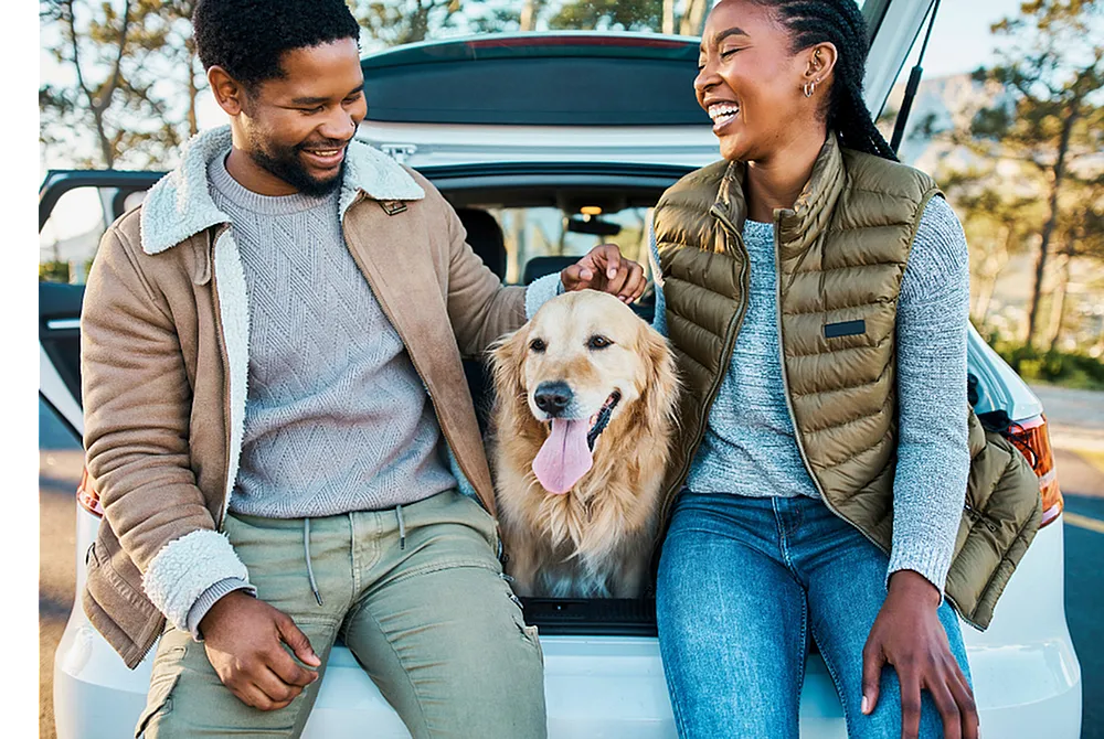Happy couple enjoying a scenic day outdoors with their golden retriever, sitting at the back of a car, exuding warmth and adventure.