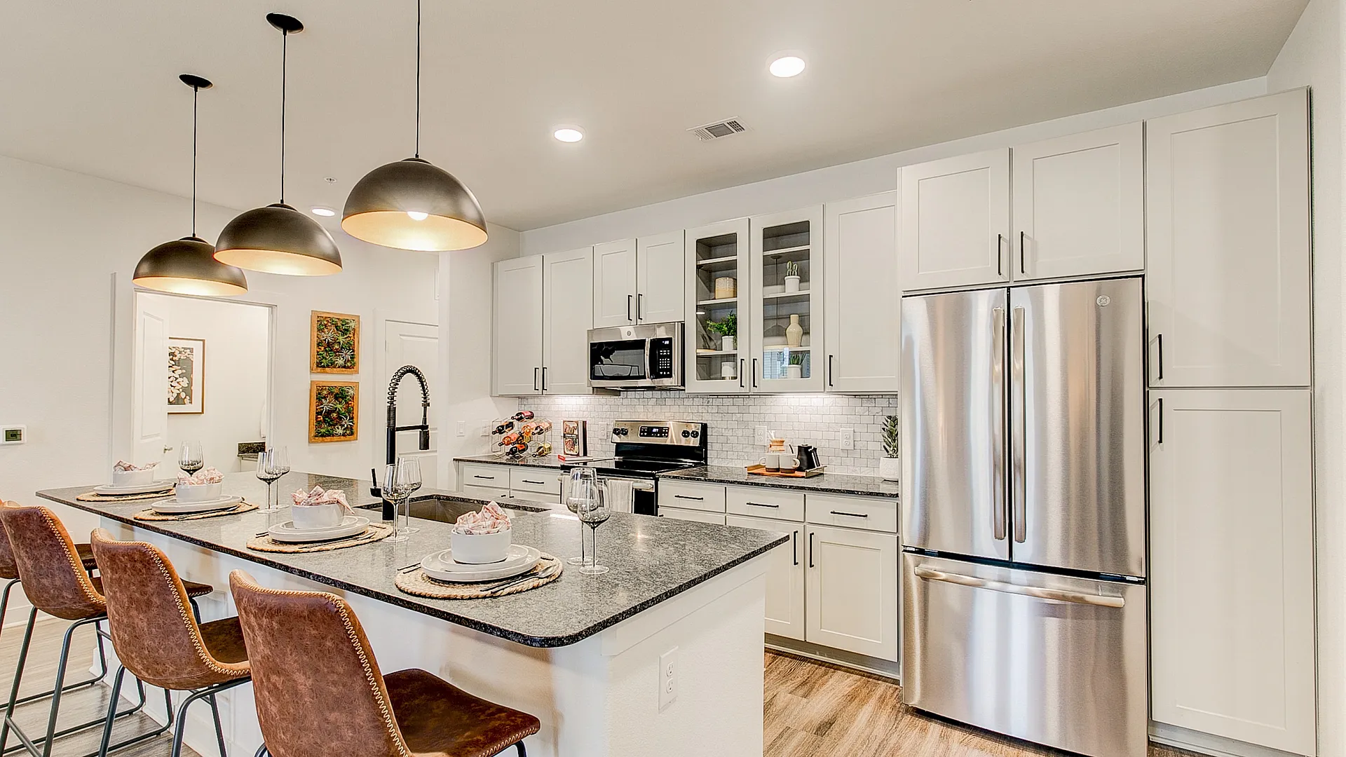 Modern kitchen with sleek white cabinets, stainless steel appliances, and an elegant island with leather bar stools and chic pendant lighting.