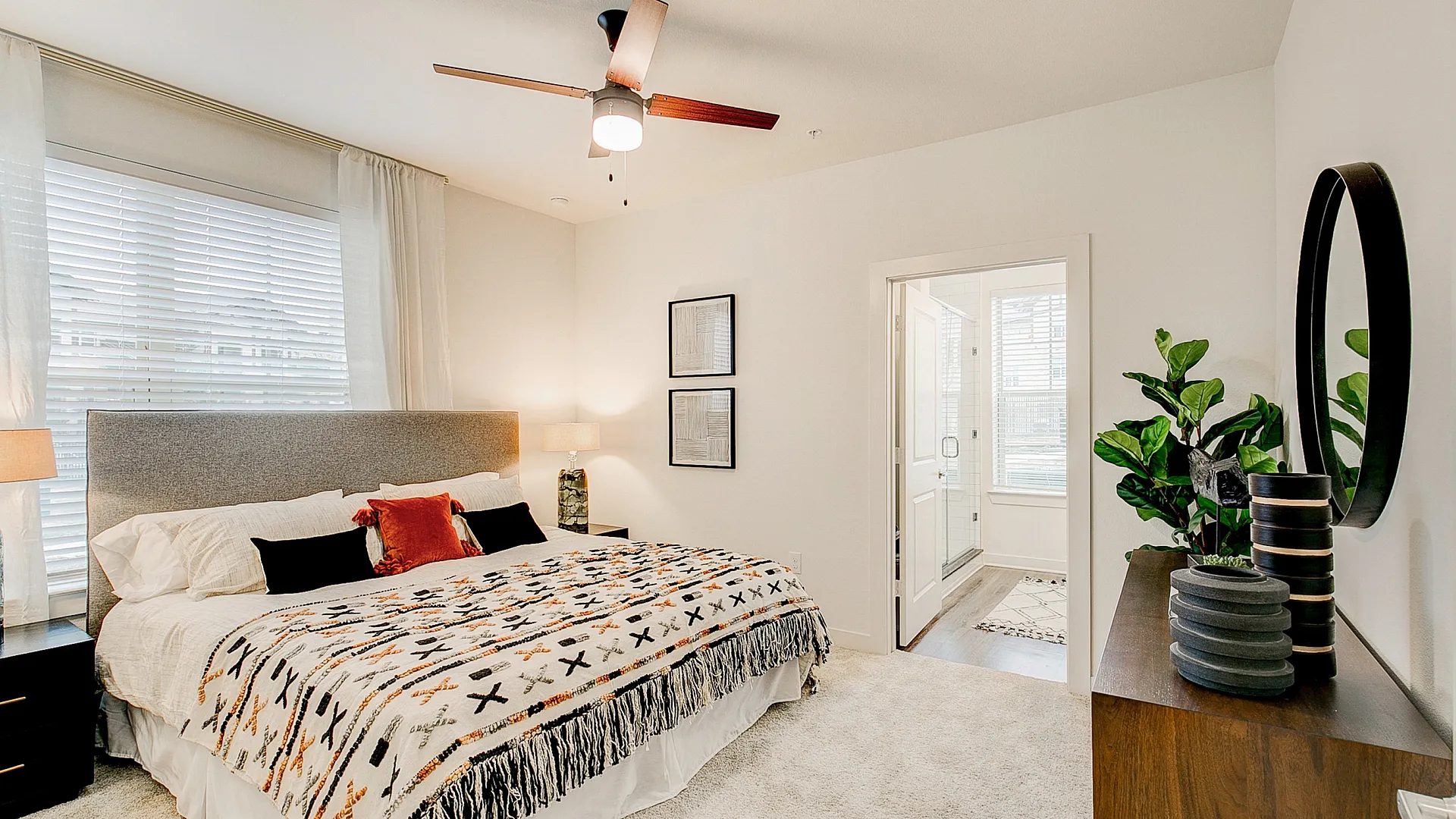 Bright and inviting bedroom featuring a cozy bed with patterned throw, large window for natural light, and modern decor with a touch of greenery.