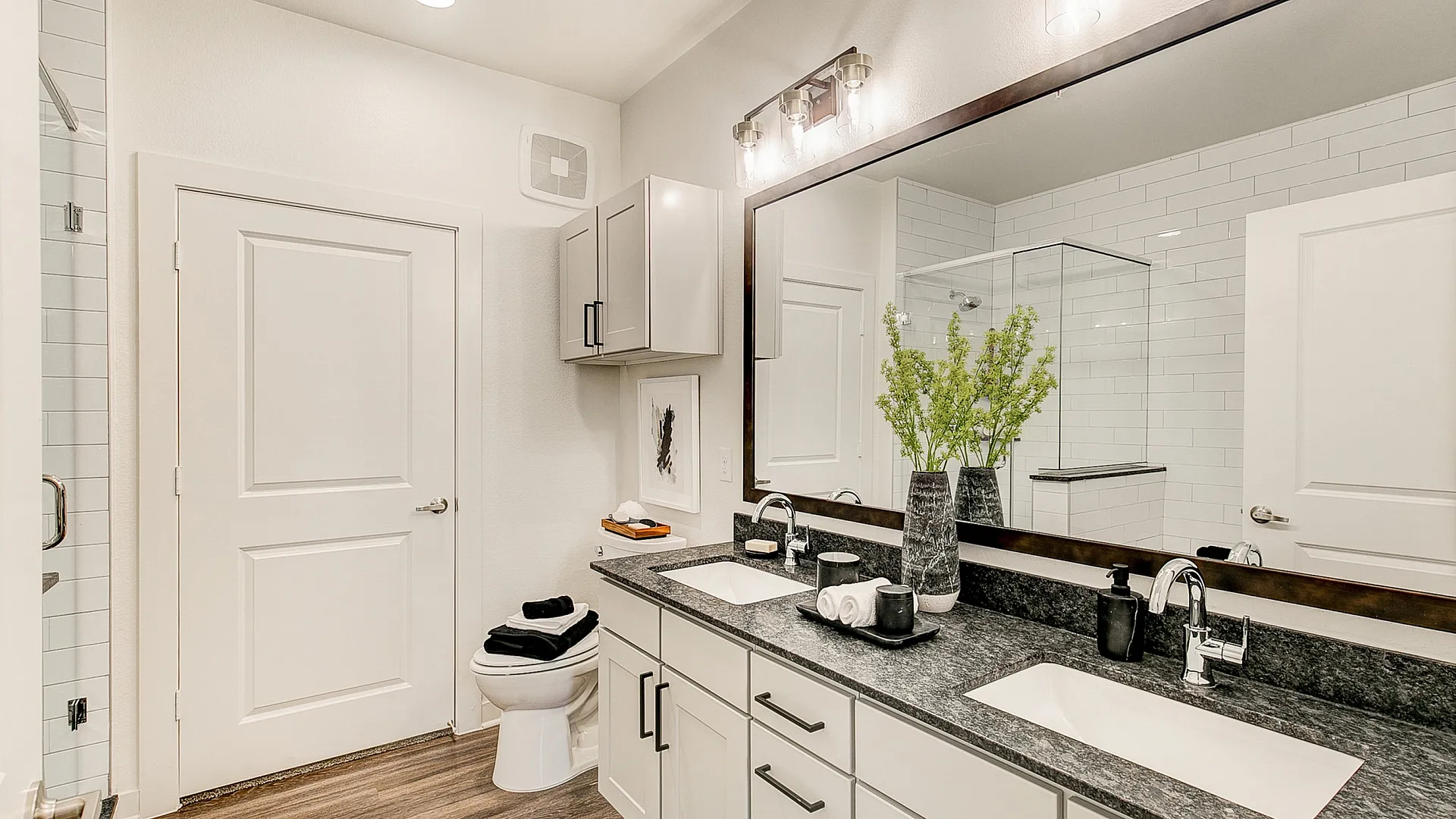 Elegant bathroom featuring a double sink vanity with modern lighting, sleek white cabinetry, and stylish decorative accents.
