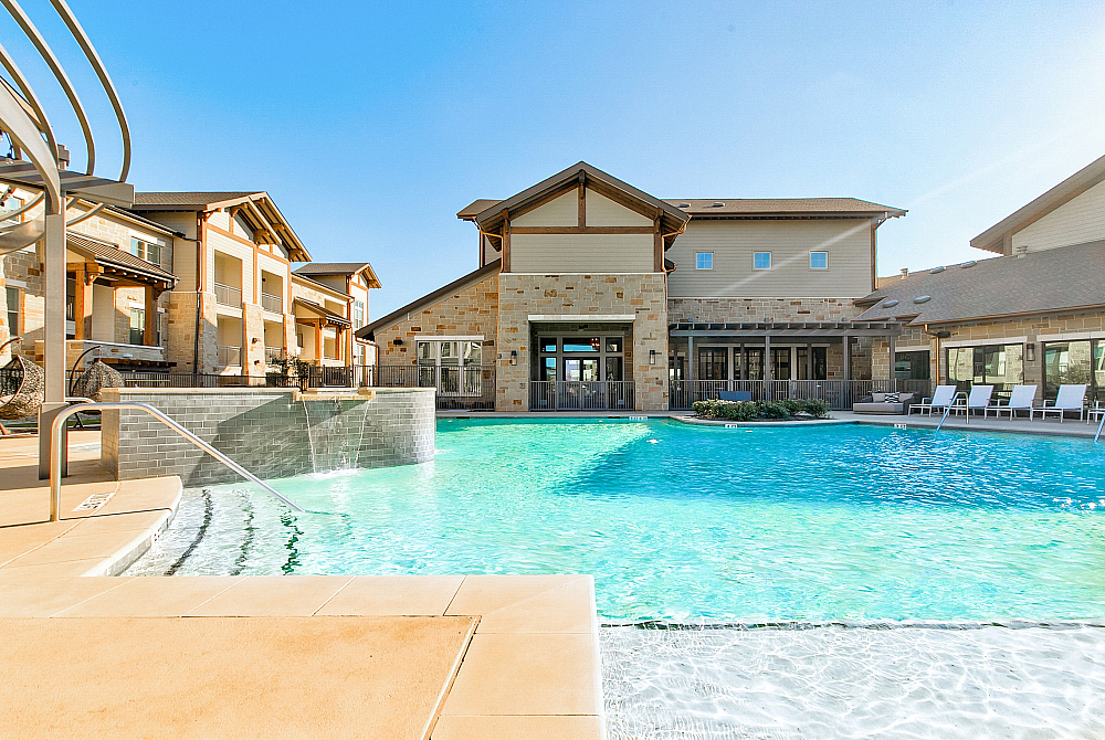 Luxurious apartment complex with a sparkling swimming pool surrounded by stylish architecture and sun loungers, perfect for relaxation.