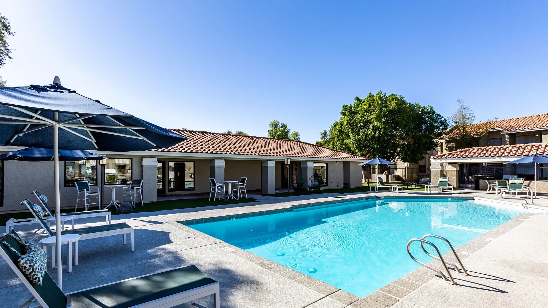 Inviting apartment complex pool area with sun loungers, umbrellas, and tranquil surroundings.