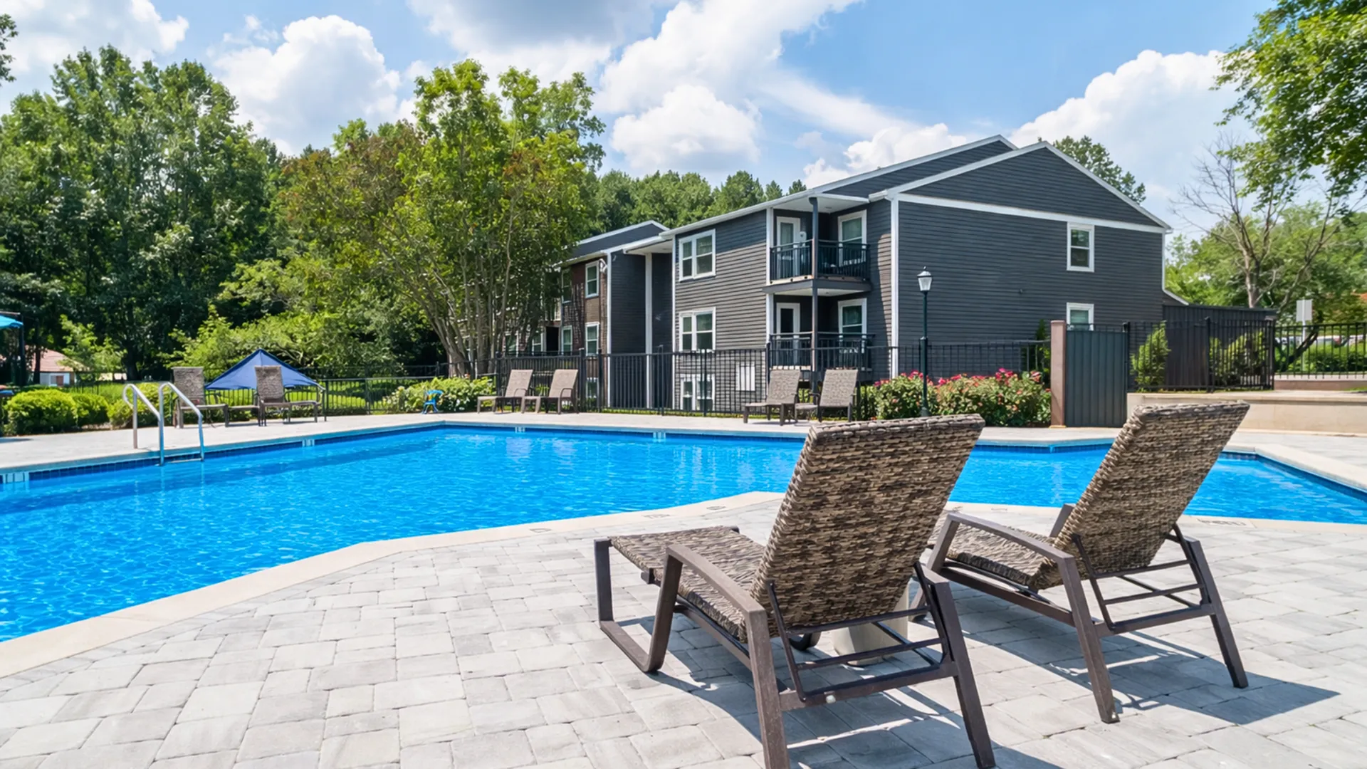 Charming residential scene with a sparkling blue pool surrounded by lush greenery and modern apartments, perfect for relaxation and leisure.