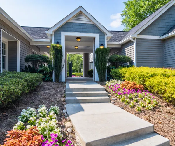 Charming residential entrance with lush landscaping, vibrant flowers, and inviting walkway leading to a stylish home.