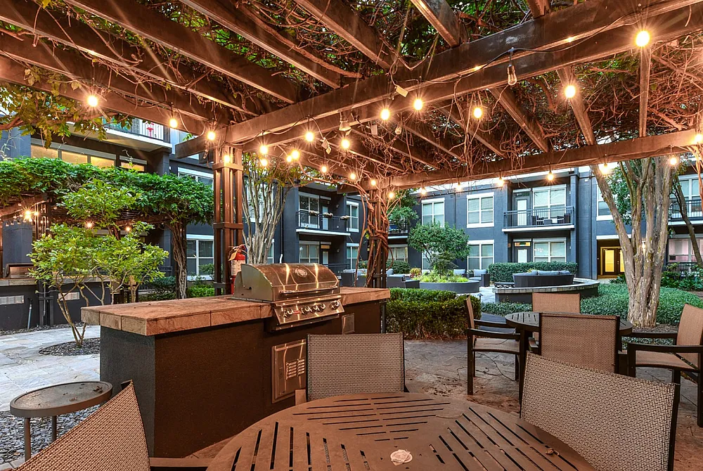 Charming outdoor courtyard with a cozy dining area, decorative string lights, and a built-in grill, perfect for evening gatherings.