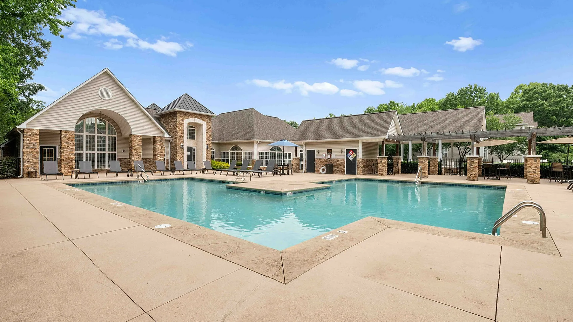 Inviting outdoor pool area with stylish lounge chairs and elegant clubhouse under a clear blue sky, perfect for relaxation and gatherings.