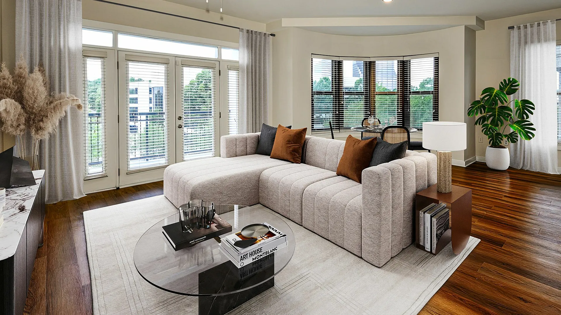 Luxurious living room with chic beige sectional sofa, glass coffee table, and modern accents, featuring hardwood floors and abundant natural light from large windows.