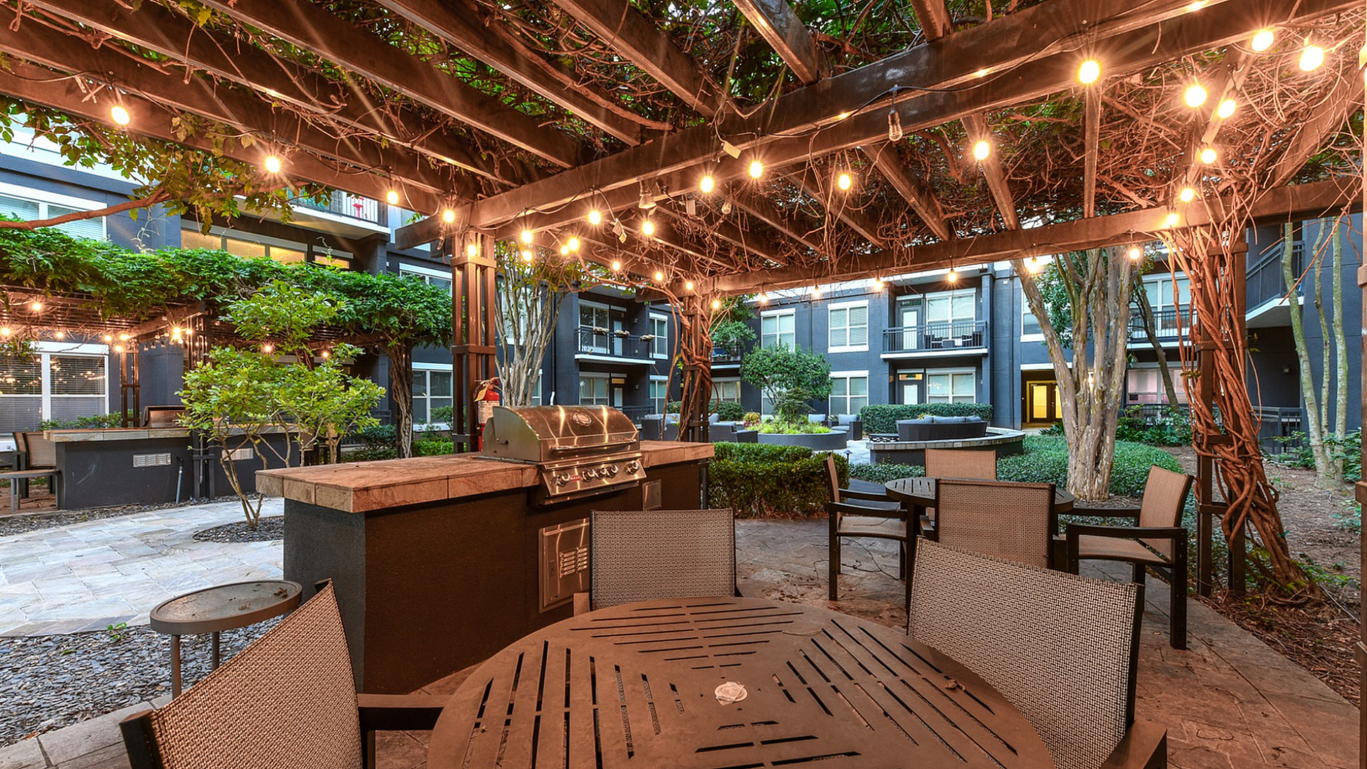 Charming outdoor patio with vine-covered pergola and twinkling string lights, featuring modern barbecue grill and stylish seating.