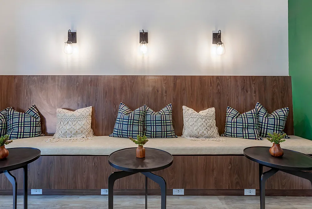 Chic seating area featuring a modern wooden bench with stylish cushions, illuminated by elegant wall sconces and accented with sleek coffee tables.