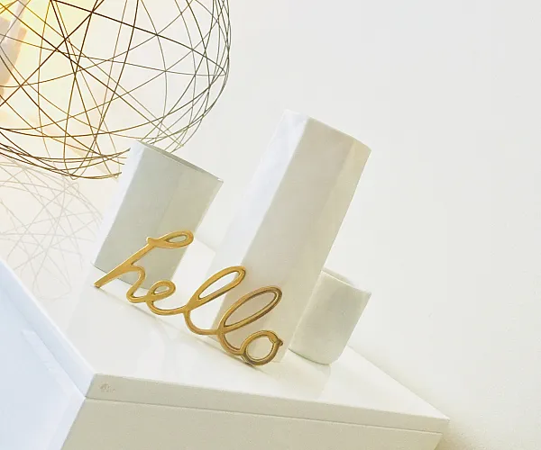 Chic modern decor featuring a white cabinet, stylish gold 'hello' ornament, and contemporary wire lamp for a welcoming ambiance.