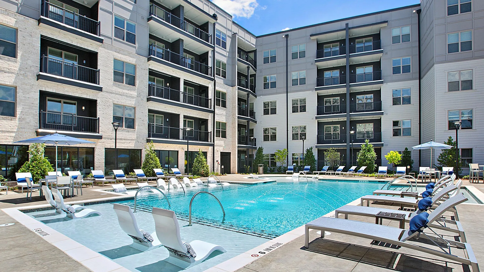 Luxurious modern apartment complex featuring a sparkling outdoor pool with stylish lounge chairs and serene poolside ambiance.