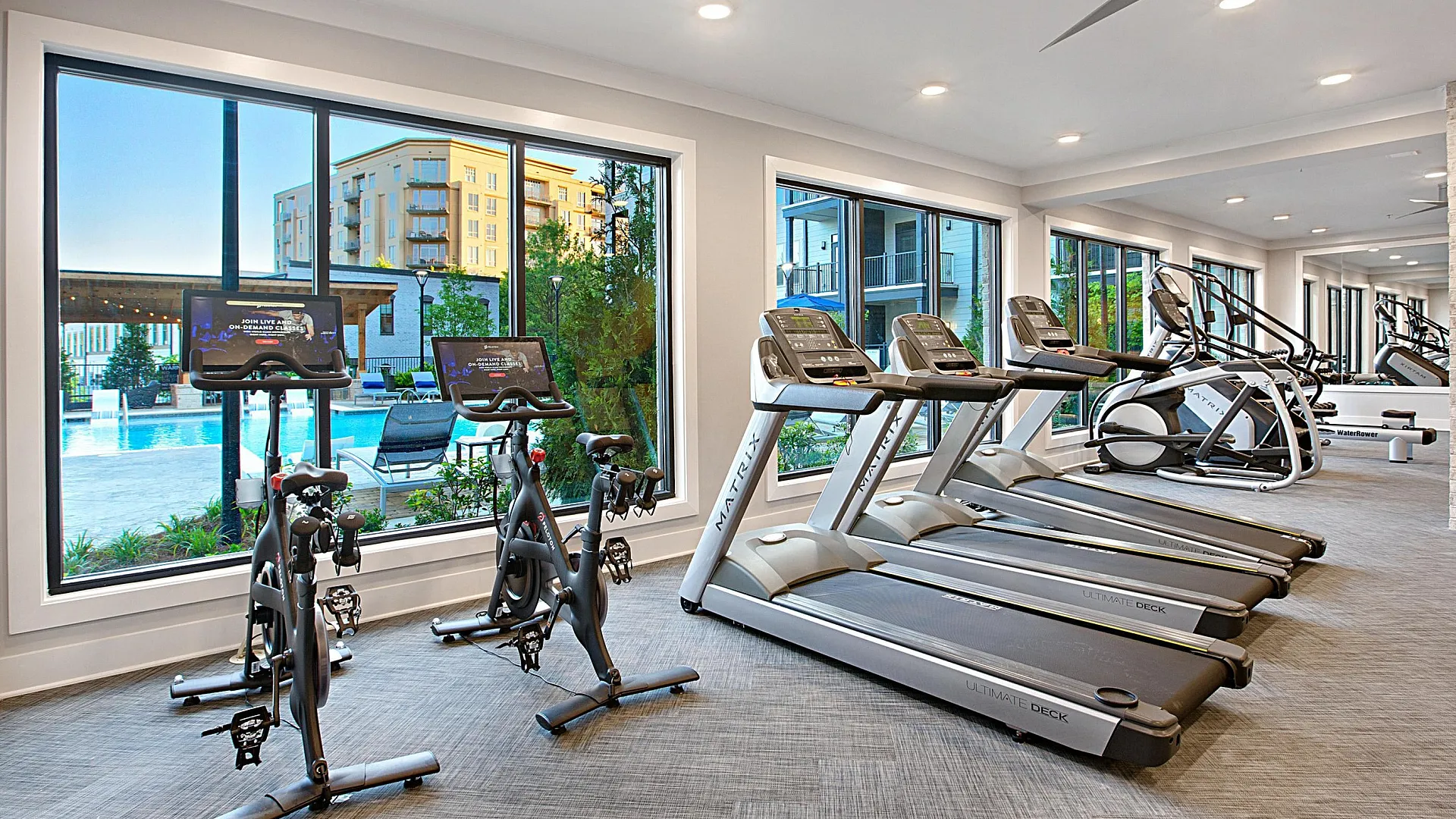 Modern fitness center featuring state-of-the-art treadmills and exercise bikes with a stunning view of the outdoor pool area.