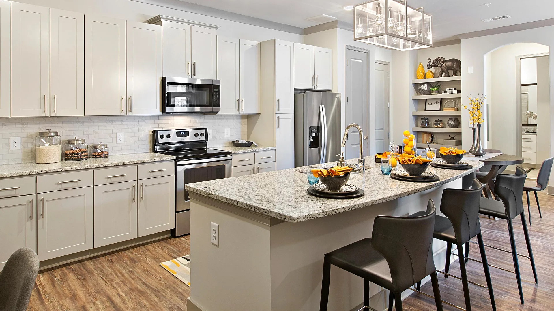 Modern kitchen with sleek granite countertops, elegant pendant lighting, and stylish black bar stools, offering ample storage with white cabinetry and stainless steel appliances.