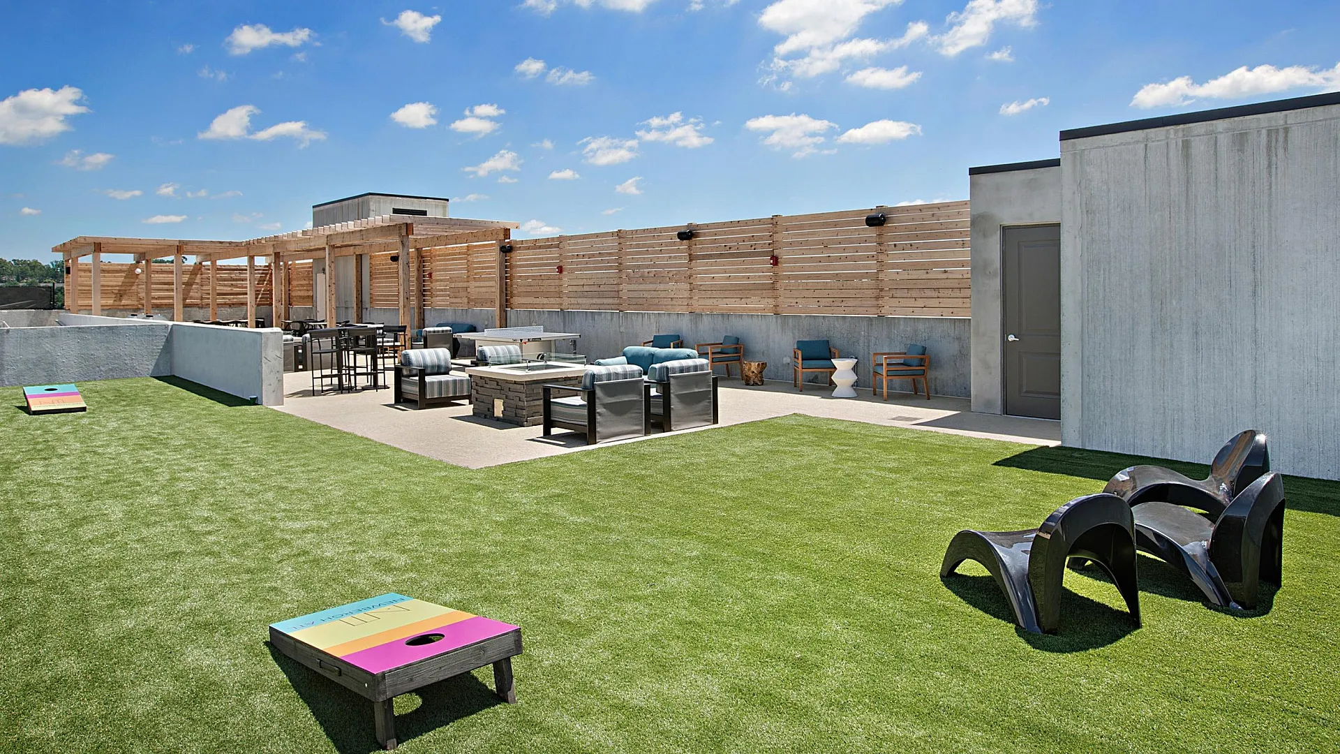 Chic rooftop oasis with cozy seating, vibrant cornhole game area, and modern pergola, offering a perfect outdoor retreat under clear blue skies.