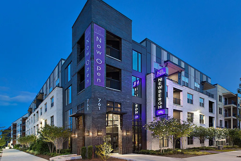 Modern apartment complex with sleek architecture, vibrant signage, and inviting greenery, highlighting the 'Now Open' status.