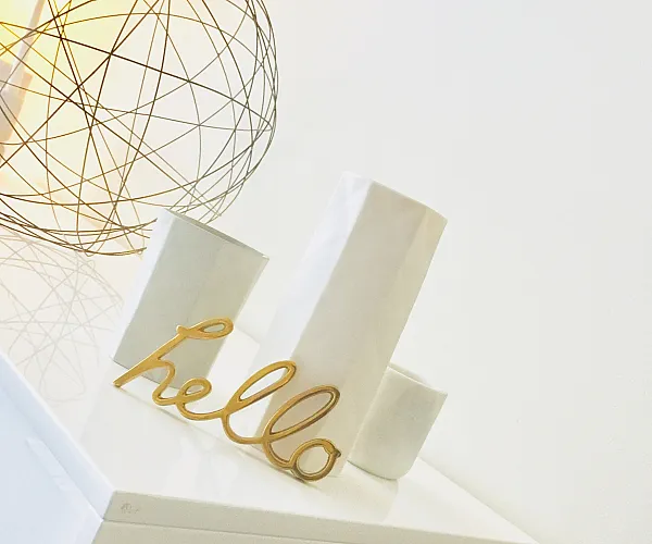 Modern interior detail with a sleek white cabinet and stylish decor, including a warm gold 'hello' sign and geometric wire lamp.