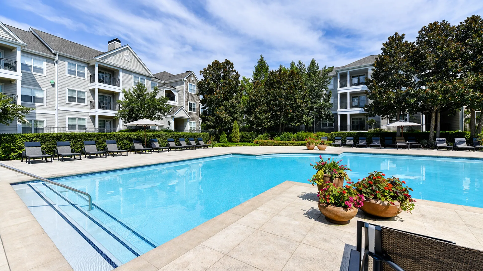 Luxurious apartment complex with a sparkling outdoor pool, surrounded by stylish lounge chairs and lush greenery, perfect for a relaxing retreat.