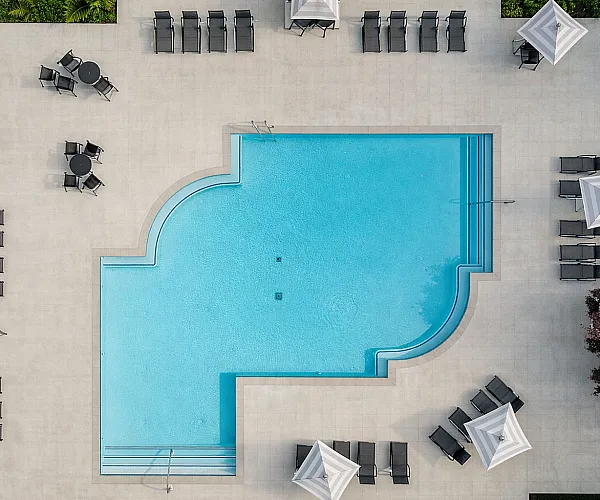 Luxurious aerial view of an elegant swimming pool with stylish loungers and chic umbrellas, surrounded by lush greenery.