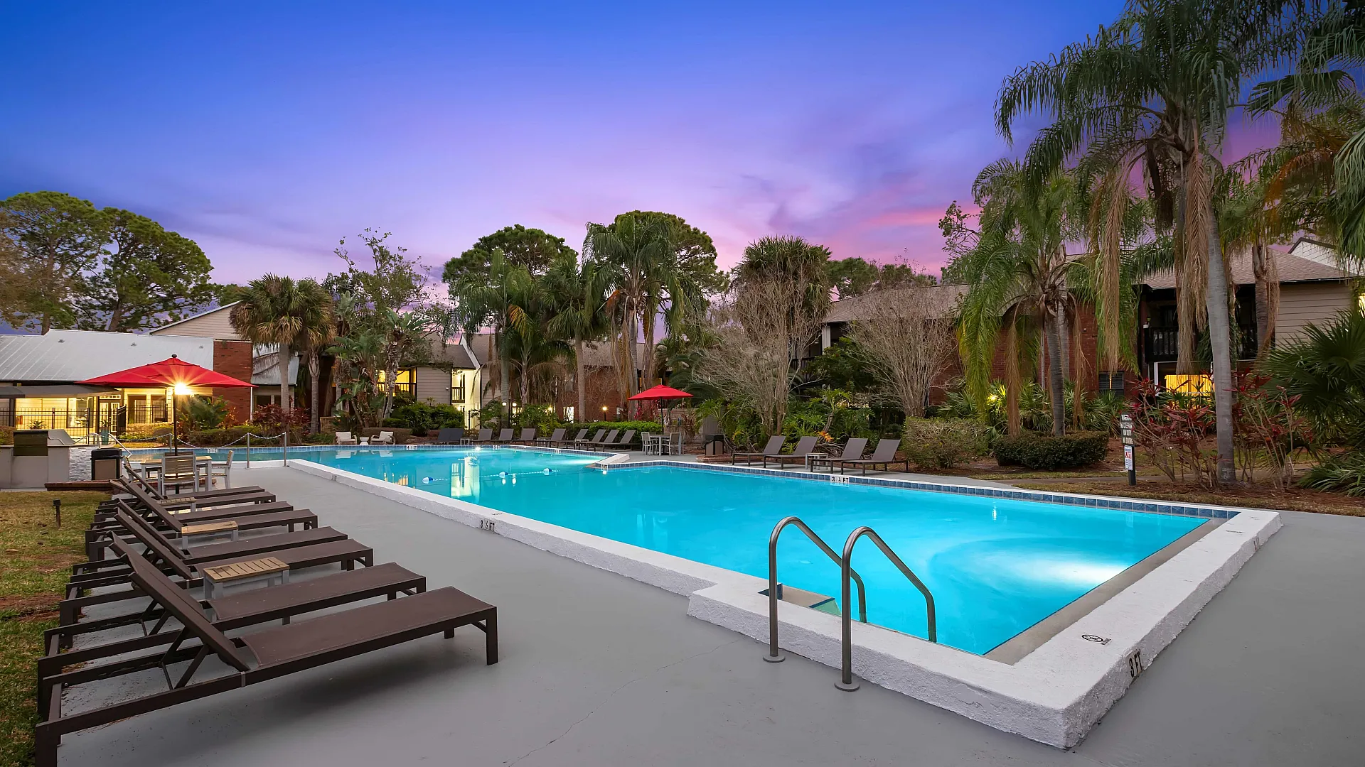 Luxurious poolside area with modern lounge chairs, surrounded by lush greenery and a serene sunset backdrop, offering a perfect retreat at this upscale property.