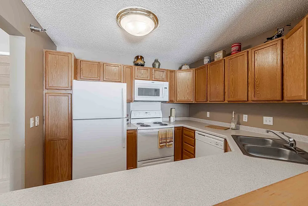 Charming kitchen with abundant wooden cabinetry, modern white appliances, and a sleek countertop inviting culinary creativity.