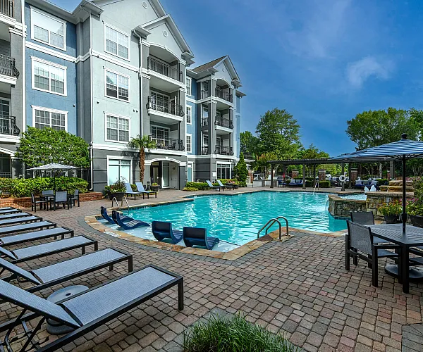 Luxurious apartment complex with a sparkling pool, comfy loungers, and elegant outdoor seating, set against a modern architectural backdrop.