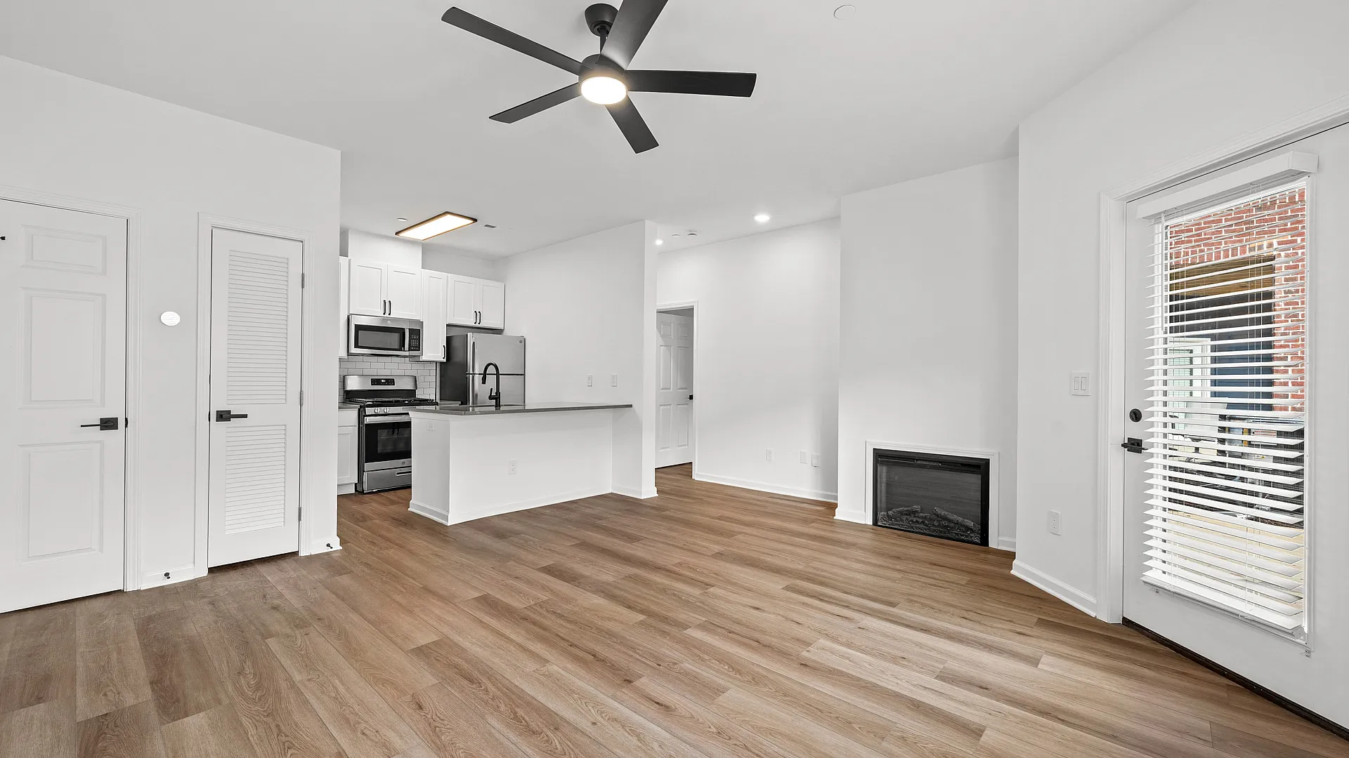 Modern open-plan living area with sleek kitchen, hardwood floors, ceiling fan, and natural light from large windows.