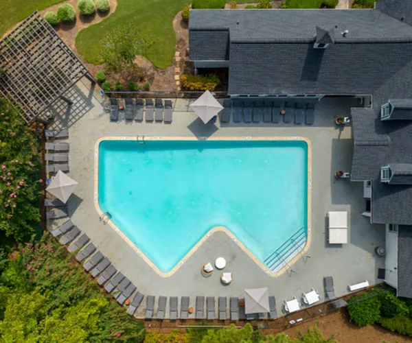 Aerial view of luxurious apartment complex with elegant pool, stylish lounge chairs, and landscaped greenery, offering a serene retreat.